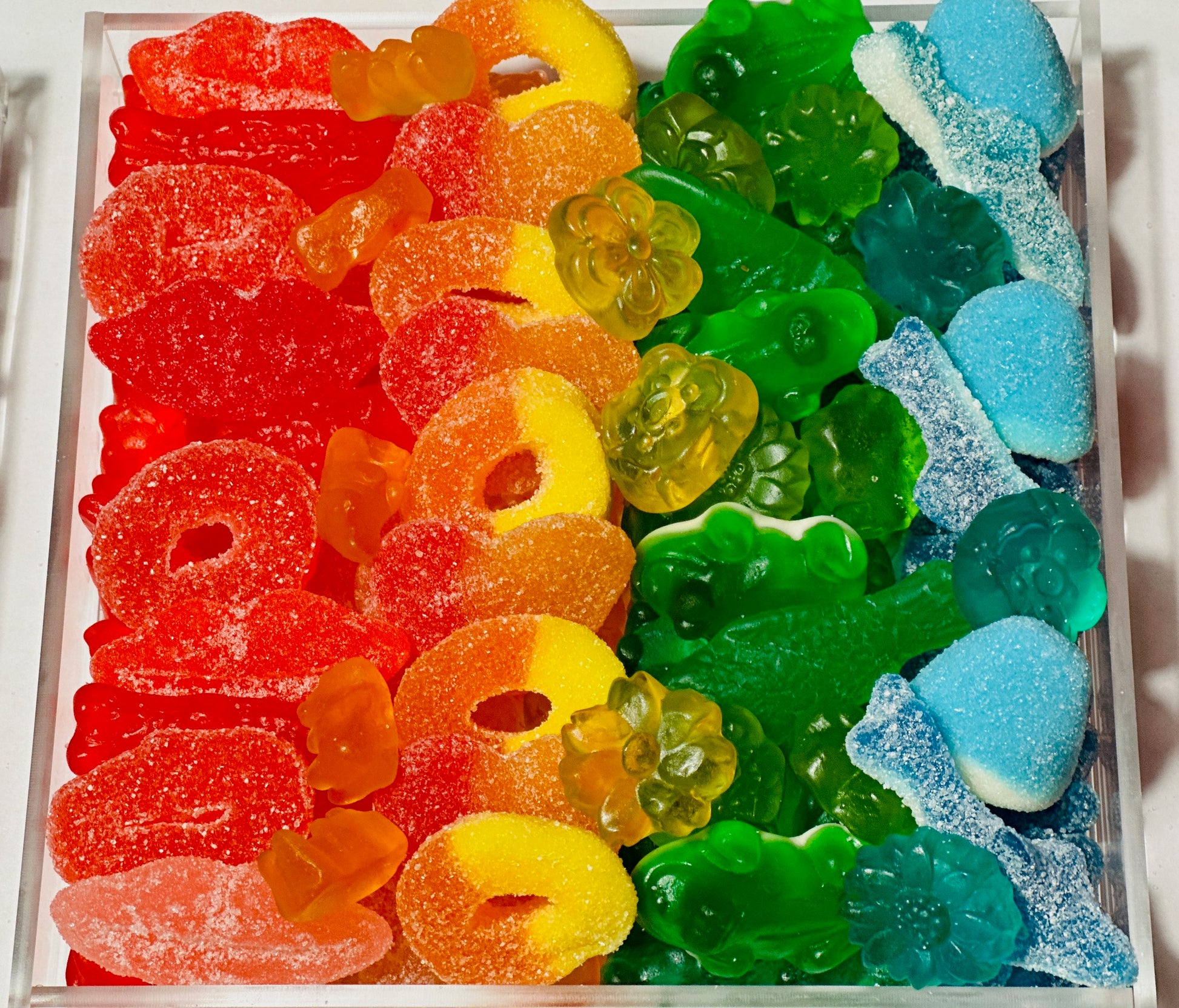 rainbow colored gummi candy board with sweet and sour lips rings sea creatures hearts butterfly flowers puffs frogs fish berry shaped gummi candy on acrylic tray that makes perfect gift for friend spouse child teen